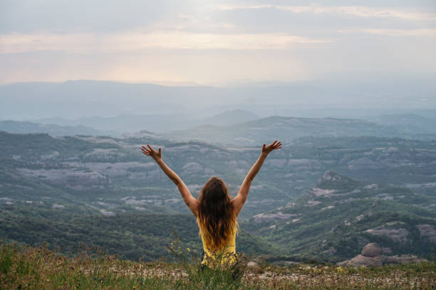 a woman stretching arms up in front of hills