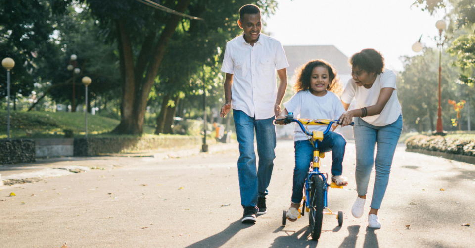 a family teaching a child to ride a bike