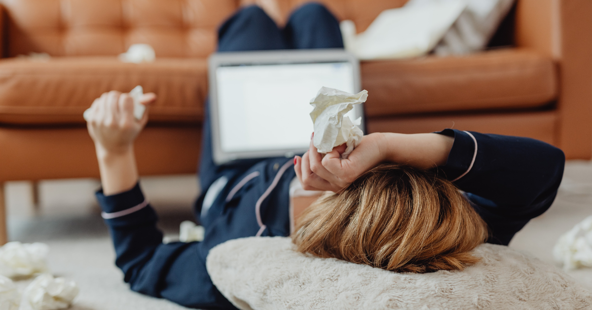 a lady with an allergy laying down with tissues on a laptop