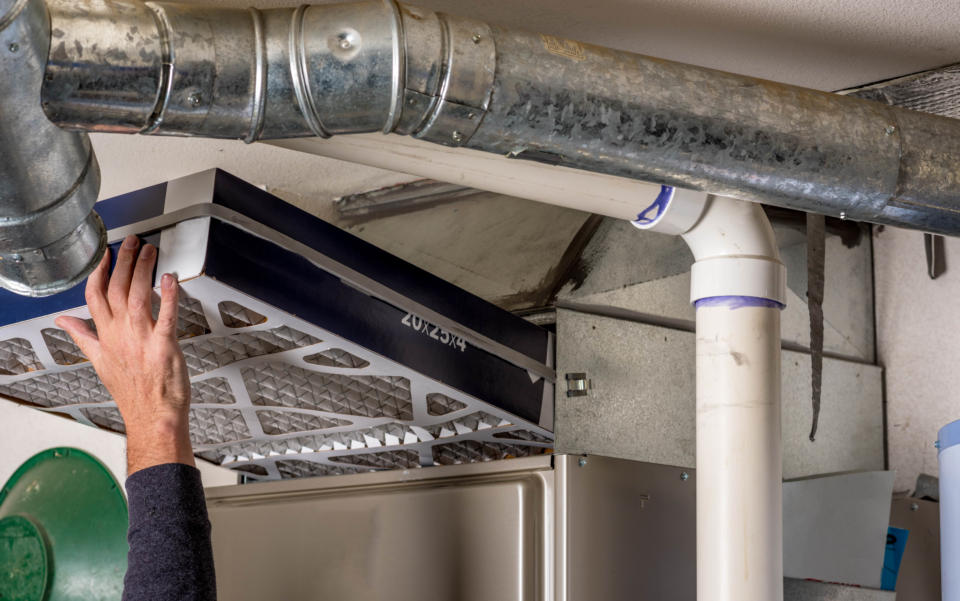 A person installing a furnace filter in a basement.