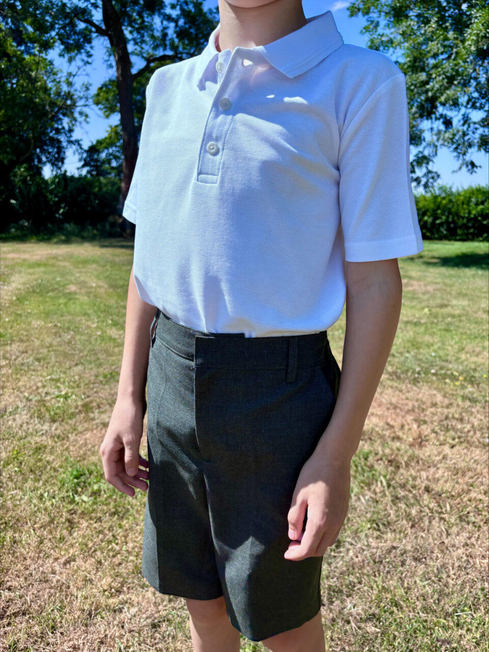 a child stood wearing a white polo shirt with shorts