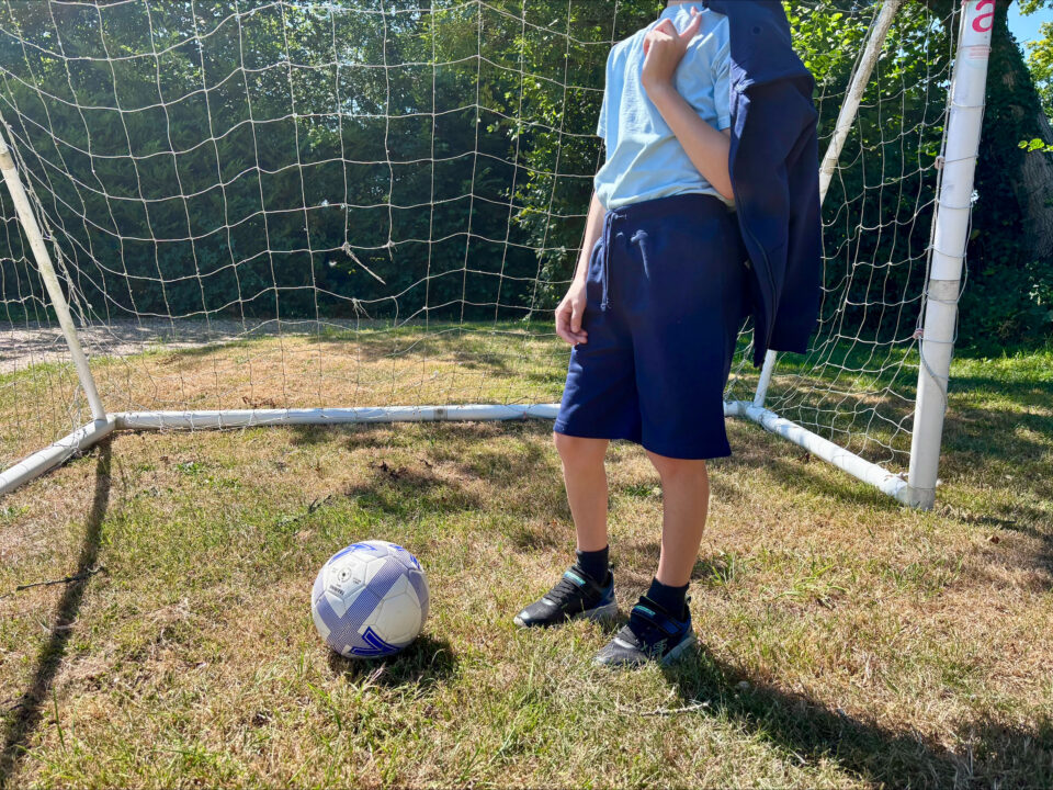 child in blue PE kit standing in a goal with a football