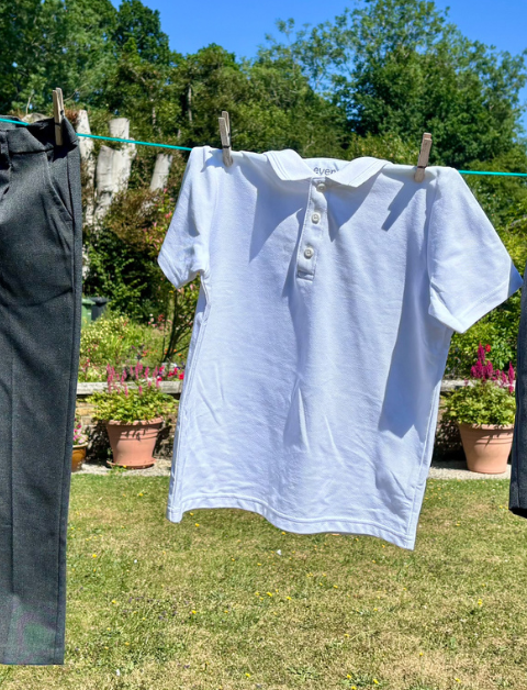 kids school uniform hanging on a line in the sunshine - white polo top, trousers and shorts