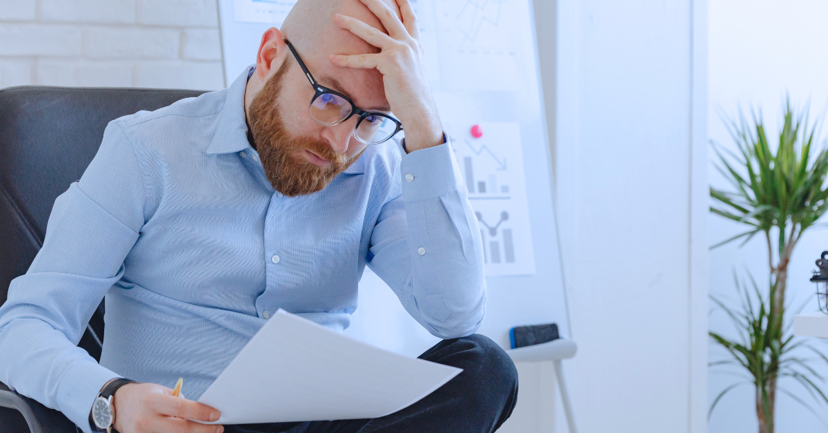 a man holding his head looking at paperwork